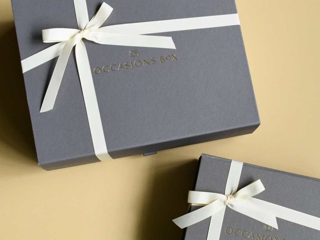 Two signature charcoal Occasions Box gift boxes with gold embossed lids and ivory ribbon